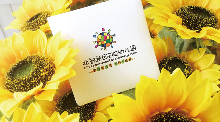 北部新区实验幼儿园物料样机,园徽卡片置于葵花花丛,教育品牌VI设计