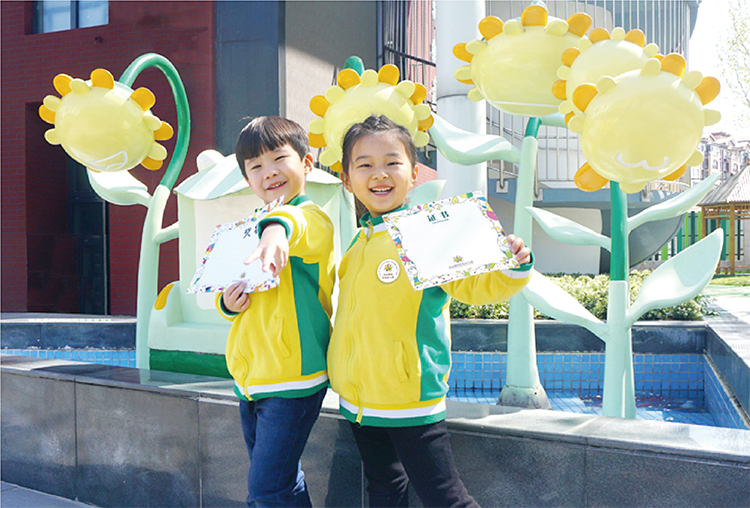 北部新区实验幼儿园孩子们身着黄绿园服拥抱葵花雕塑的活动照片，园所景观文化