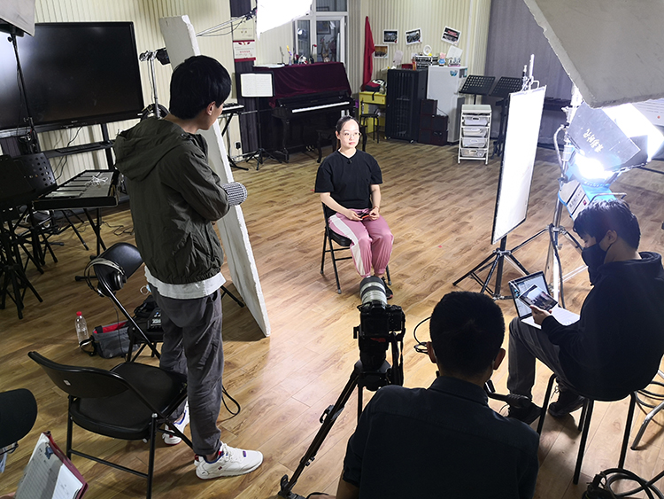 锦连环团队在红英小学拍摄人物采访现场，摄像灯光设备环绕受访者，文化视频制作