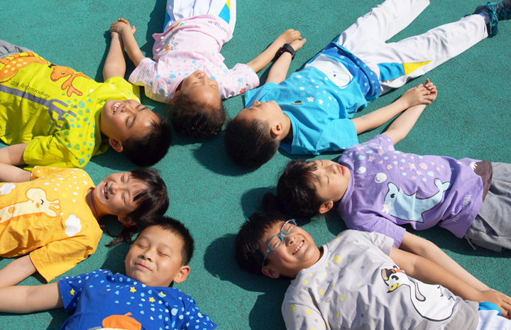 红英小学学生身穿七彩阳光战袍围圈躺地，展现阳光岛校园文化活力氛围