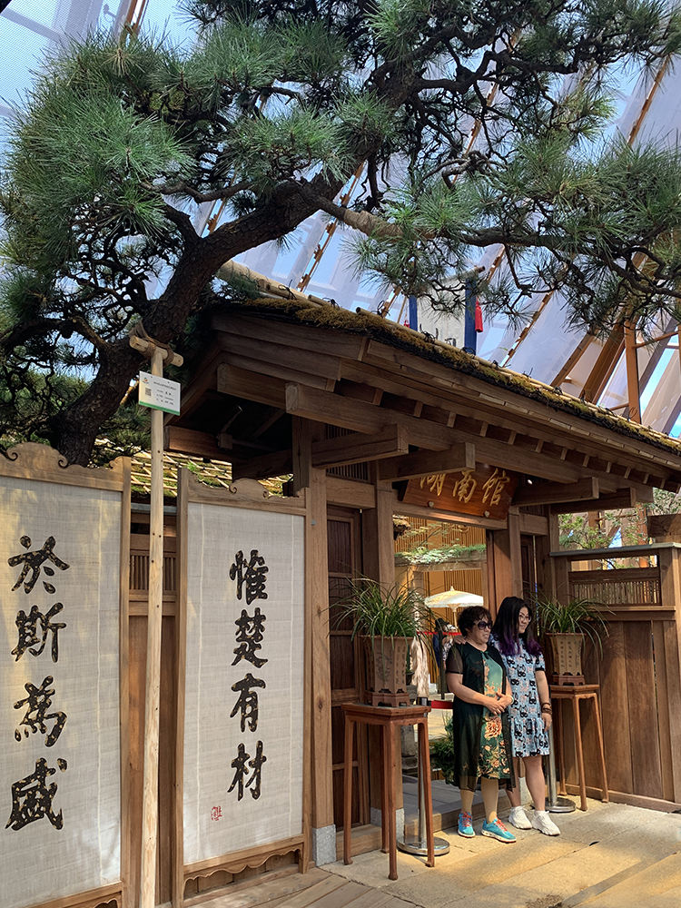 世园会湖南展园传统门楼，古松掩映，门柱悬惟楚有材楹联，游客驻足观赏