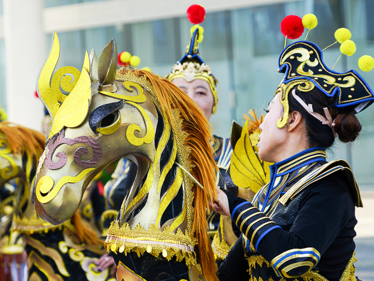 世园会巡游演出，演员佩戴金色骏马造型头饰与华丽戏装，民俗表演热闹