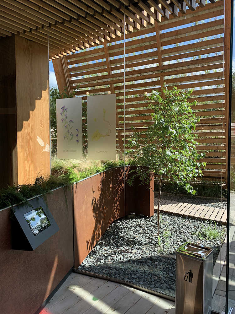 世园会展园木格栅庭院，绿树与卵石景观相映，展板讲述园艺主题，造景清雅