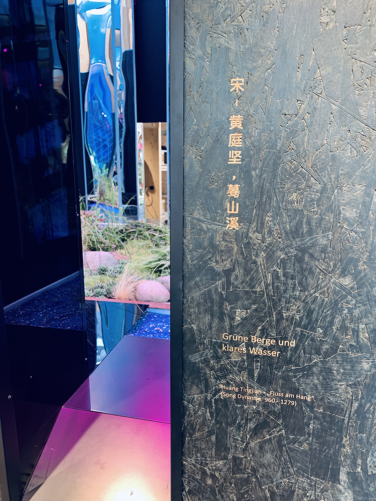世园会深色展墙呈现宋代黄庭坚题刻图文，幽蓝水景映衬，展现植物文化底蕴