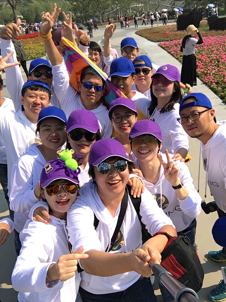 锦连环团队身着白衫头戴紫帽，于世园会花海前欢呼合影，活力四射