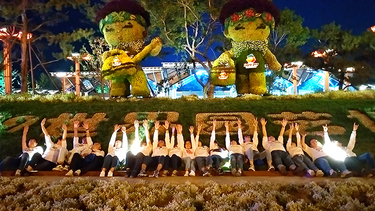 夜幕下世园会绿植造型景观前，锦连环团队列队合影，灯光璀璨气氛热烈
