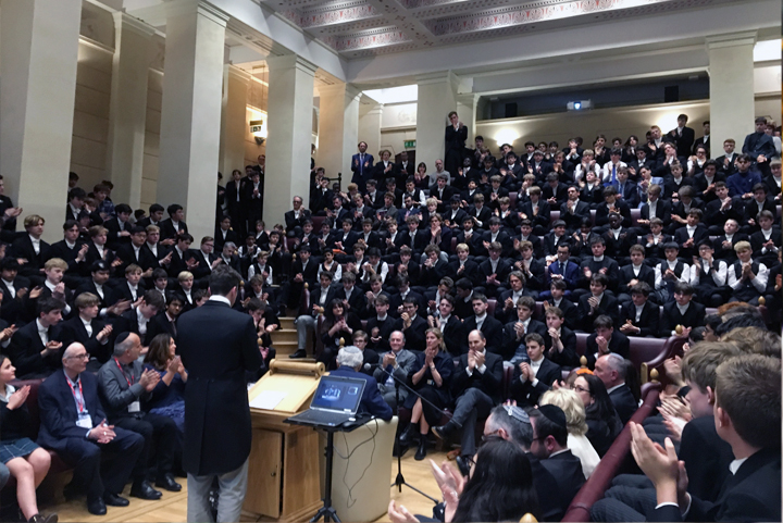 伊顿公学礼堂内众多身穿校服的学生列席集会聆听演讲，体现学校规章秩序与集体文化