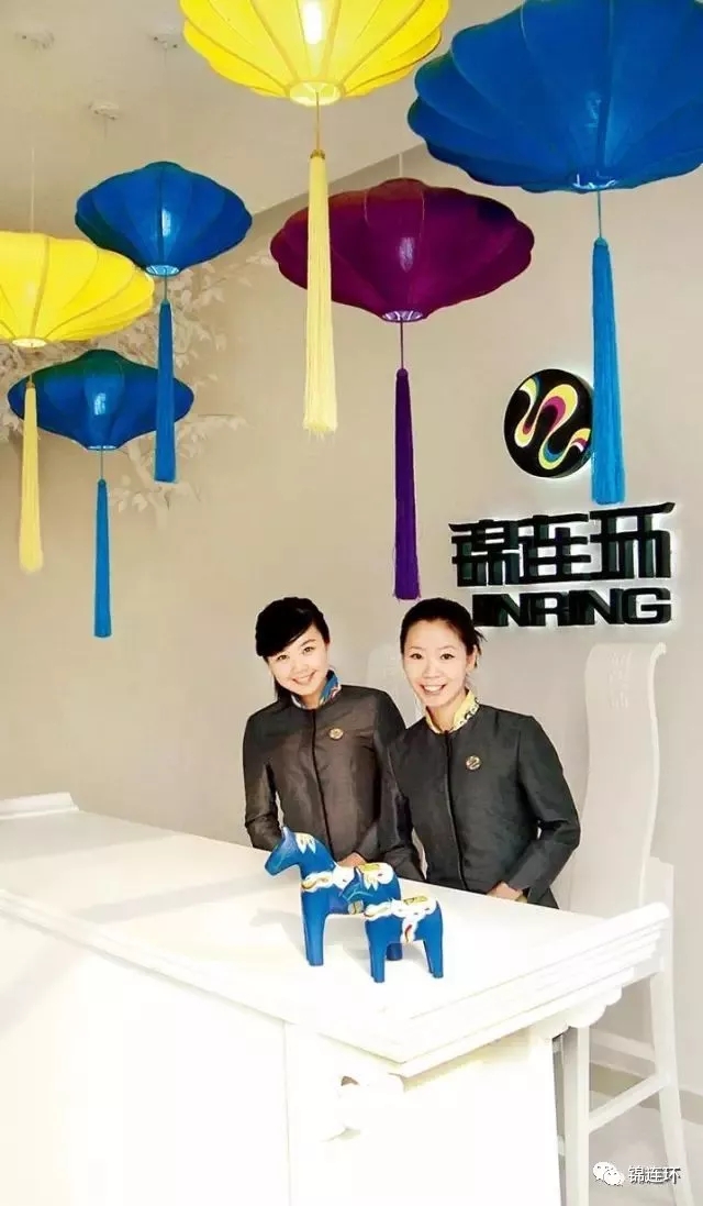 锦连环两位员工在品牌形象墙前的合影，顶部彩色伞饰，呈现公司接待与办公空间氛围