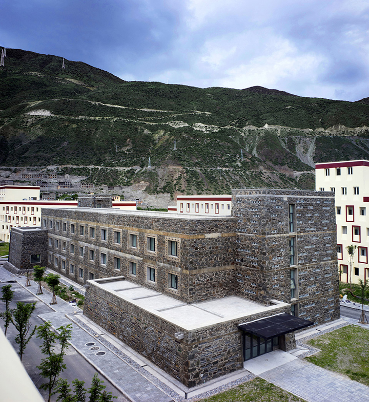 依山而建的山区学校教学楼日景，石材外墙与群山融为一体，体现自然第一的校园建筑设计