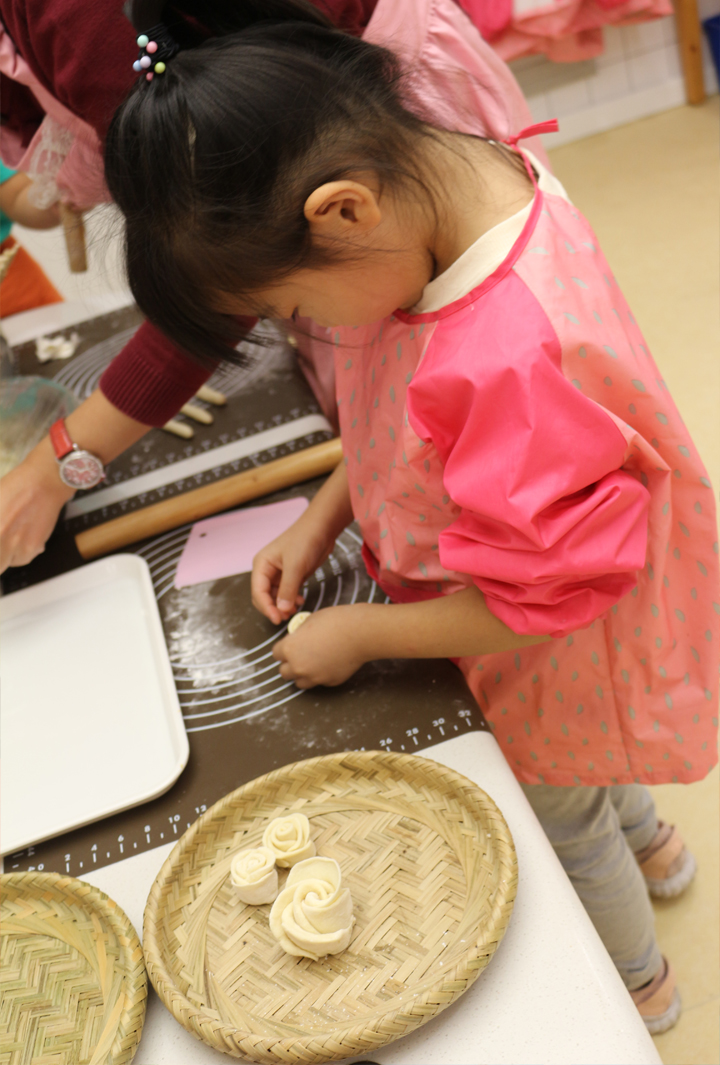 立新幼儿园小朋友身穿粉色围裙擀面制作面点，体验生活教育烹饪课程