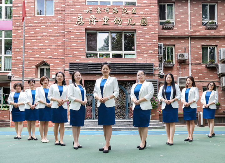 恩济里幼儿园教师身着蓝色职业装在园所教学楼前列队合影，展现师资团队风采