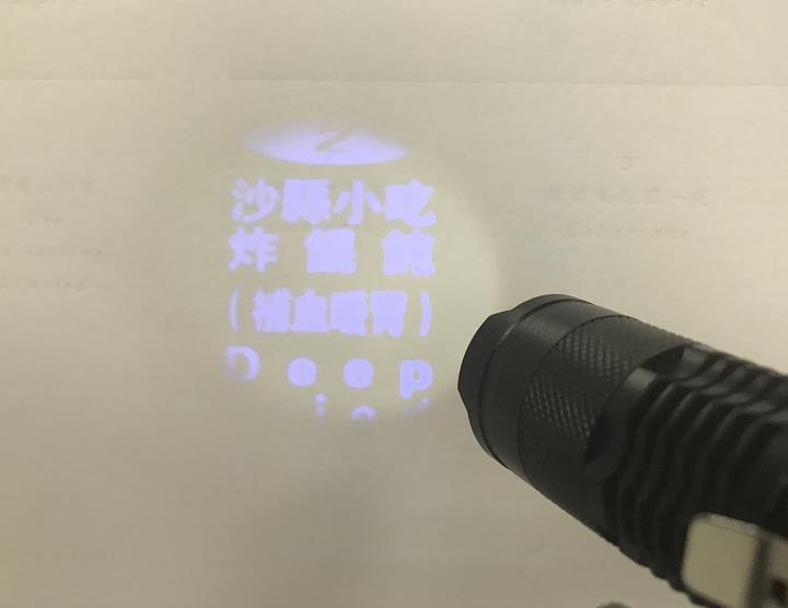 投影手电将沙县小吃趣味文字投射于纸面，体现笔记本内页丰富精彩的创意互动巧思