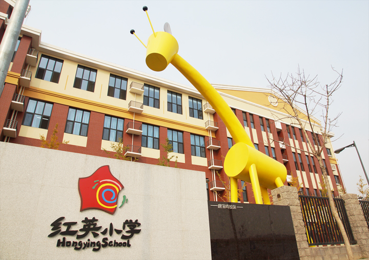 红英小学教学楼外景，黄色长颈鹿雕塑矗立门前，墙面镶嵌红英小学校徽与校名标识