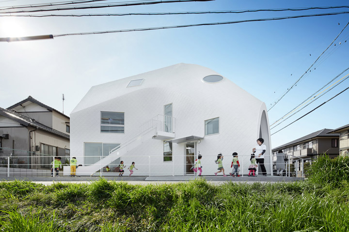 四叶草之家幼儿园白色沥青帐篷状建筑外景,孩子们在前方活动,体现幼儿园环境建设轻盈阳光的氛围