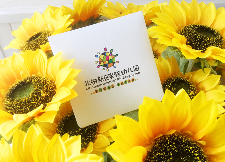 北部新区实验幼儿园品牌设计应用,向日葵丛中摆放印有园所标志的卡片,呼应葵花森林主题校园文化