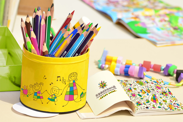 北部新区实验幼儿园文具用品VI应用,黄色笔筒印有儿童插画与园徽,搭配彩色铅笔与绘本,体现教育品牌设计