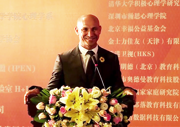 一位外籍男嘉宾在积极心理学大会演讲台微笑发言的场景