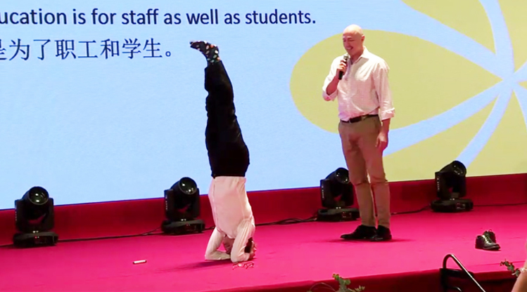 一位外籍嘉宾在大会舞台倒立演讲,大屏显示教育为了职工和学生