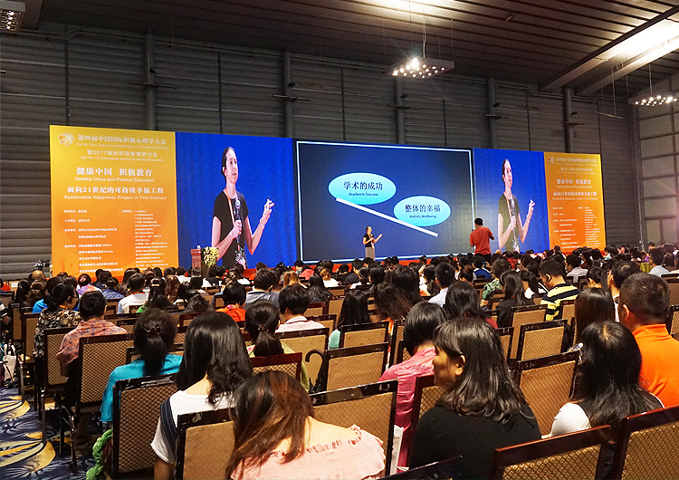 积极心理学大会会场后排观众与远处舞台演讲场景的全景