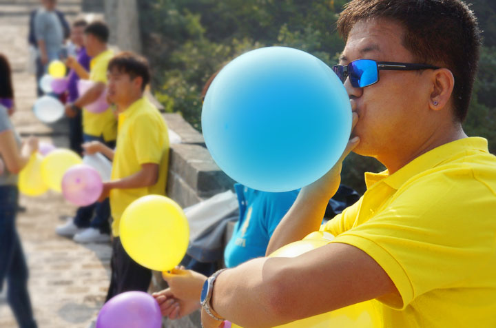 身着黄色队服的锦连环成员在长城上吹气球，趣味互动其乐融融