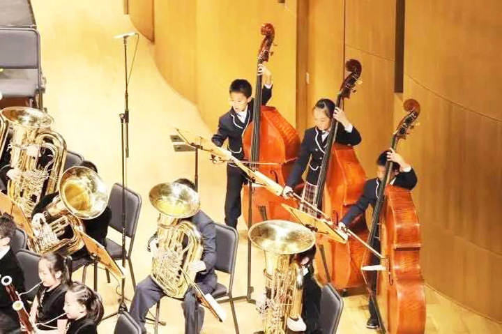 北京石油附小学生管乐团身着演出服合奏铜管与弦乐器,校园艺术教育现场