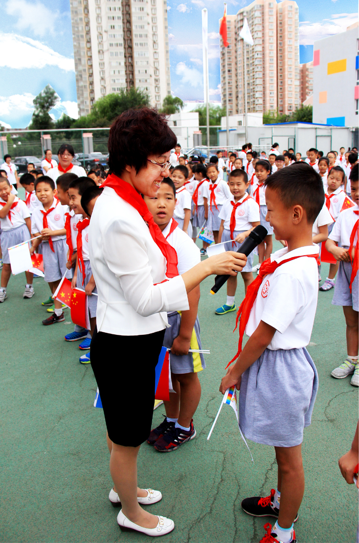 西二旗小学开学典礼,女教师手持话筒与戴红领巾学生互动交流,锦连环旗趣文化校园活动现场