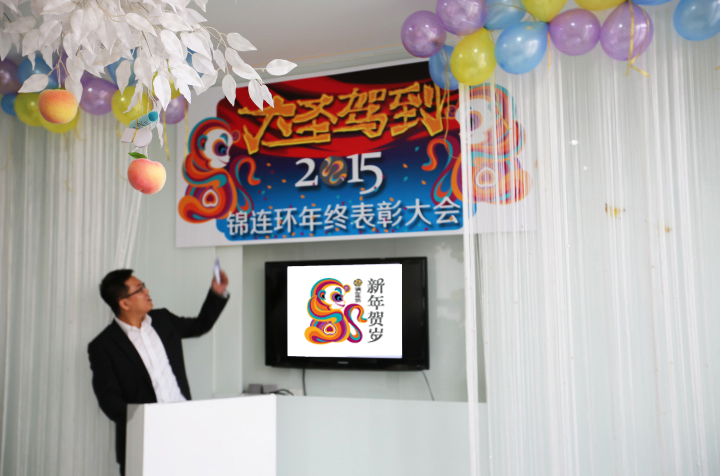 锦连环2015年终表彰大会现场,主持人站在写有年会主题的背景墙前发言