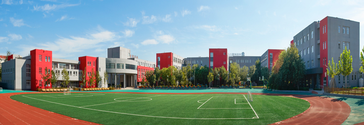 中关村第二小学校园全景，红灰教学楼环绕绿茵运动场，锦连环校园环境建设